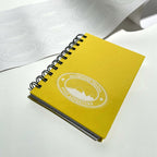 Clear round label with white underprint applied to a yellow notebook